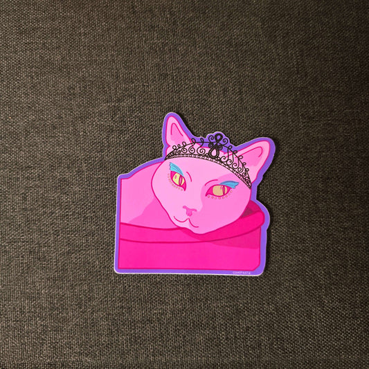 princess cat wearing black diamond tiara with blue eyeliner lounging in a pink cat bed